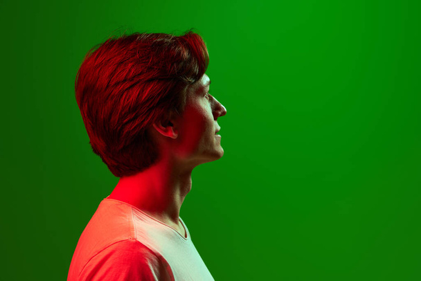 Sakin ol, Pasifik. Profil görüntüsü, yeşil neon arka planda beyaz tişört giyen yakışıklı bir genç. İnsan duyguları kavramı, yüz ifadesi, ruh hali, iş, reklam - Fotoğraf, Görsel