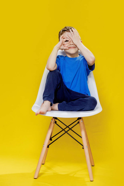 Cheerful Little Boy Sitting on Yellow Chair - Bright and Playful Portrait. - 写真・画像