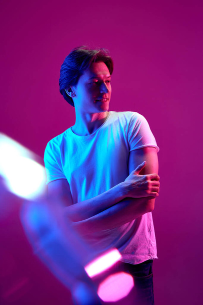 Personal space. One young guy, man with calm face standing and looking away over pink background in neon light. Solitude. Concept of youth, human emotions, facial expression, ad - Photo, Image
