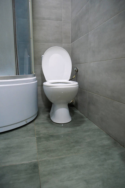 WC-szoba belseje fehér WC-csészével, zuhanykabinnal és szürke falburkolattal - Fotó, kép