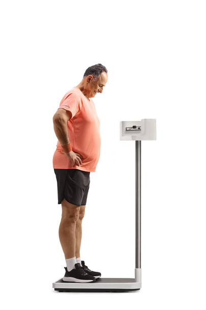 Mature man standing on a medical weight scale and looking down isolated on white background - Фото, зображення