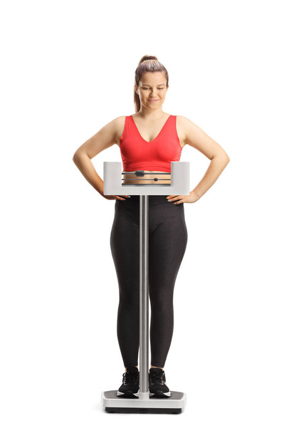 Young woman in sportswear weighing on a medical scale and smiling isolated on white background - Photo, Image