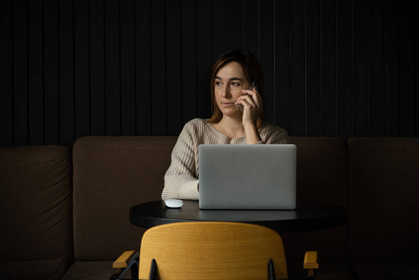 Όμορφη καυκάσια γυναίκα συγκεντρωμένη ενώ χρησιμοποιεί φορητό υπολογιστή σε ένα σύγχρονο χώρο εργασίας. Χαριτωμένη νεαρή επιχειρηματίας μιλάει στο τηλέφωνο - Φωτογραφία, εικόνα
