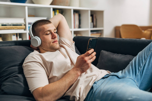 A caucasian man uses his mart phone and lays on the sofa - 写真・画像