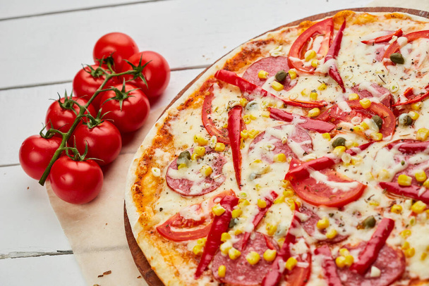 Čerstvě upečená chutná papriková pizza se salámem, sýrem mozzarella, kukuřicí a pepřem podávaná na dřevěném pozadí s rajčaty, omáčkou a bylinkami. Koncept dodávky jídla. Menu restaurace - Fotografie, Obrázek