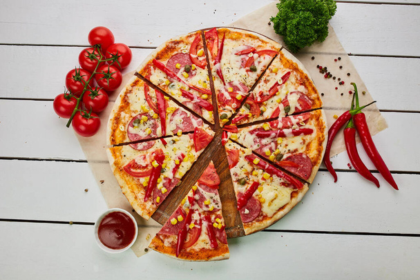Salamlı, mozzarella peynirli, mısır ve biberli taze pişmiş pepperoni pizza ahşap arka planda domates, sos ve bitkilerle servis ediliyor. Yemek teslimatı konsepti. Restoran menüsü - Fotoğraf, Görsel