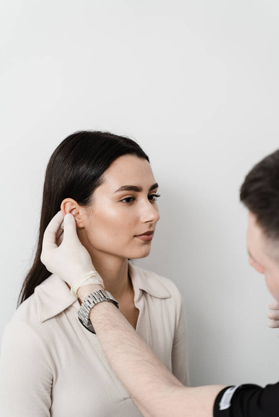 Otoplasty is surgical reshaping of the pinna, or outer ear for correcting an irregularity and improving appearance. Surgeon doctor examines girl ear before otoplasty cosmetic surgery - Foto, immagini