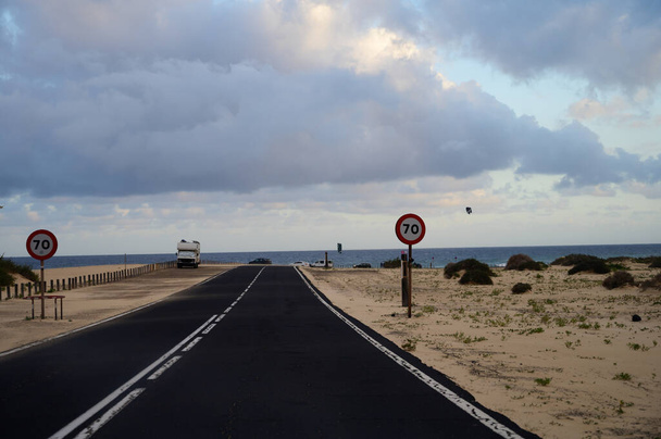 Driving car on black asphalt road through white sandy dunes near Corallejo beach at colorful sunset Fuerteventura, Canary islands, Spain - Photo, image