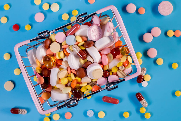 Various capsules, pills and medicines in a shopping cart on a blue background. Health care, treatment. The concept of buying pills and buying medicine. - Photo, image