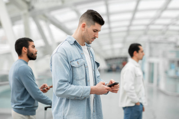 Man met behulp van Smartphone Staande in de rij met andere passagiers die wachten op vlucht in de moderne luchthaven Terminal Binnenshuis. Travel Mobile Application Advertentie. Selectieve focus - Foto, afbeelding