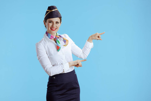 smiling elegant air hostess woman on blue background in uniform pointing at something. - Фото, изображение