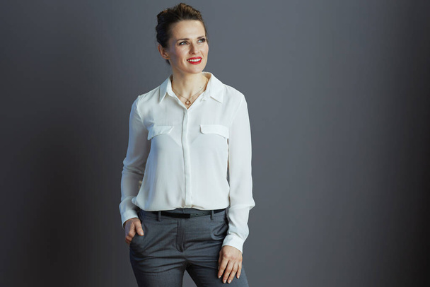 pensive elegant 40 years old woman employee in white blouse looking at copy space isolated on grey background. - Zdjęcie, obraz