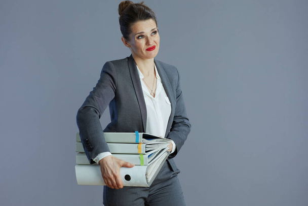 stressed modern 40 years old woman employee in gray suit with folders against gray background. - 写真・画像