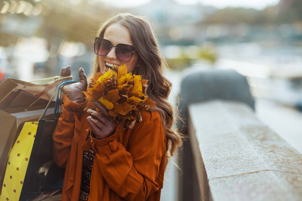 Hello autumn. happy modern woman in orange trench coat with shopping bags and autumn yellow leaves in the city. - Valokuva, kuva