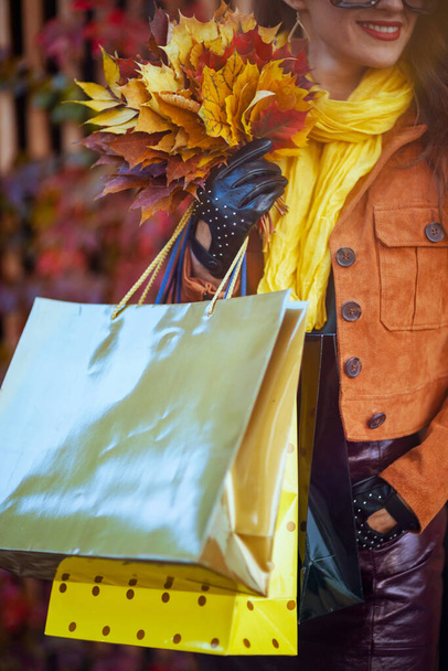 Hello october. smiling 40 years old woman in orange trench coat with shopping bags and autumn yellow leaves in the city. - Фото, зображення