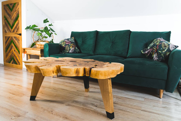 Beautiful one of a kind wooden table made by professional carpenter artist standing in living room in front of emerald sofa. High quality photo - Фото, изображение
