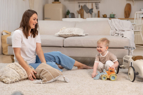 Happy family at home. Mother and baby boy playing with toys at home indoors. Little toddler child and babysitter nanny having fun together. Young woman mom kid son rest in living room - Photo, Image