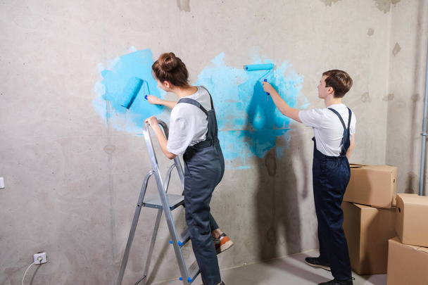 Ev dekorasyonu yenileme konsepti. Yeni ev boyama duvarının boş odasında birlikte mutlu bir çift. Karı koca ellerinde boya rulosu tutuyorlar. Yeni evde duvarları mavi boyayla boyuyorlar. - Fotoğraf, Görsel