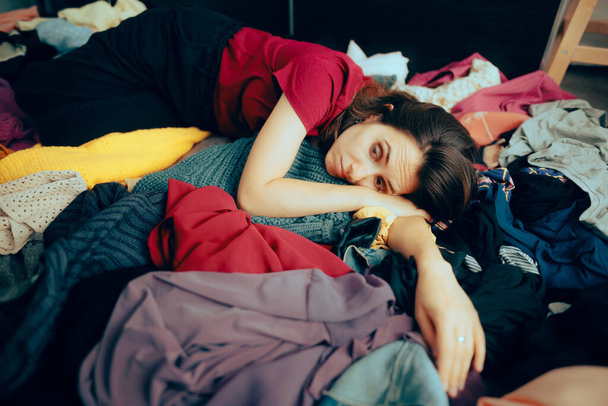 Unhappy Woman Sitting on a Pile of Clothes Having Nothing to Wear - Photo, image
