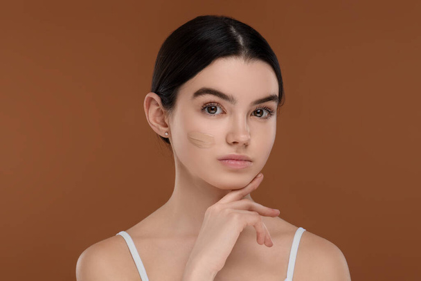 Teenage girl with swatch of foundation on face against brown background - Fotoğraf, Görsel