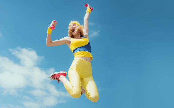 Sporty woman jumping with dumbbells. Funny woman in sportswear on sky background. Dynamic movement. Sport and healthy lifestyle Fitness woman - Valokuva, kuva