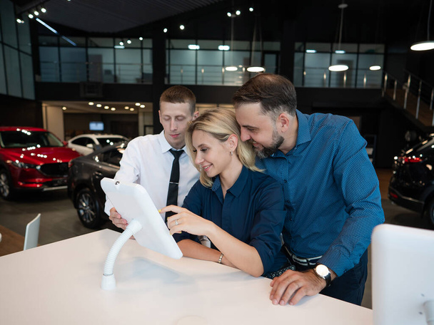 Caucasian married couple chooses a car in a car dealership on digital tablets - Fotoğraf, Görsel