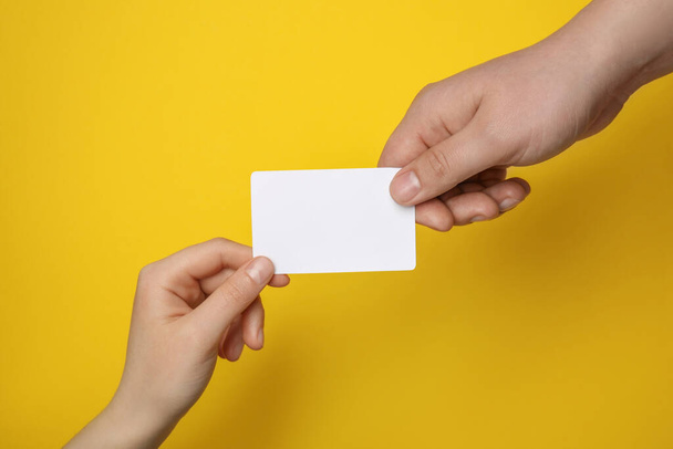 Man and woman holding blank gift card on yellow background, closeup - Fotoğraf, Görsel