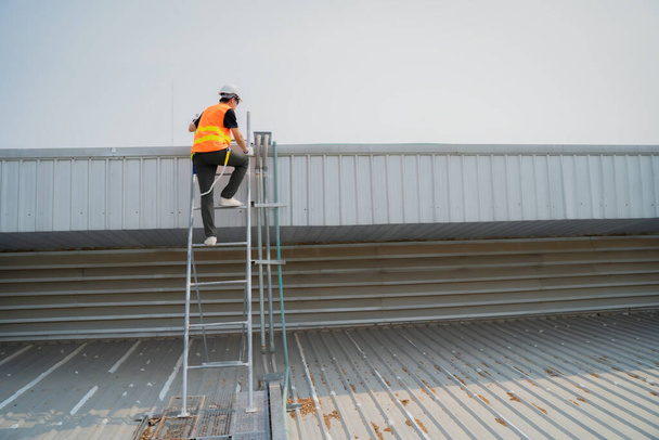 Ingeniero asiático que usa ropa protectora y una escalera blanca de hardhat que sube abajo después de terminar el trabajo. - Foto, imagen