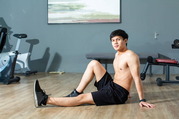 Azjatycki przystojny młody mężczyzna rozgrzewa swoje ciało, rozciągając nogi patrząc na aparat w centrum fitness. - Zdjęcie, obraz