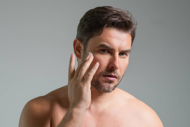 Close up portrait of man 40s applying cream on face. Handsome serious man enjoy fresh perfect skin, applying cream. Portrait of beauty man with cosmetic cream on skin. Facial treatment. male beauty - Foto, immagini