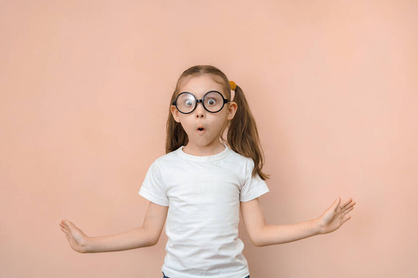 Zaskoczona dziewczyna 7 lat w okrągłych okularach na różowym tle z 2 pustymi przestrzeniami. - Zdjęcie, obraz