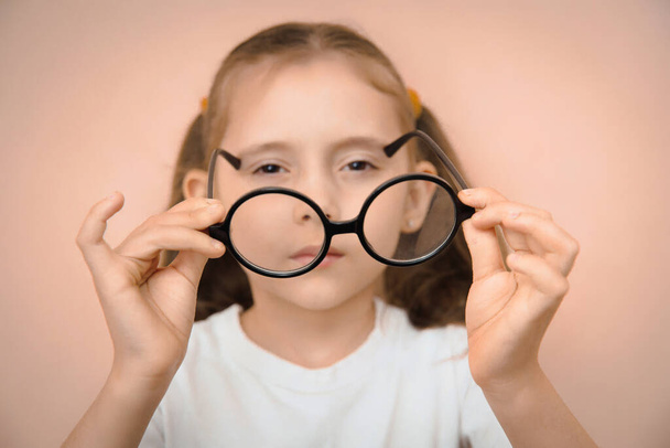 Una niña pequeña de la escuela primaria para elegir las gafas adecuadas con un dioptrador. - Foto, imagen