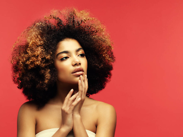 Young beautiful african american woman with afro hair. Glamour makeup. Red Background - Foto, imagen