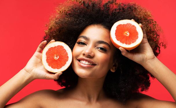 Young afro american woman hold grape slices look amazed isolated on red color background. Close up. - 写真・画像