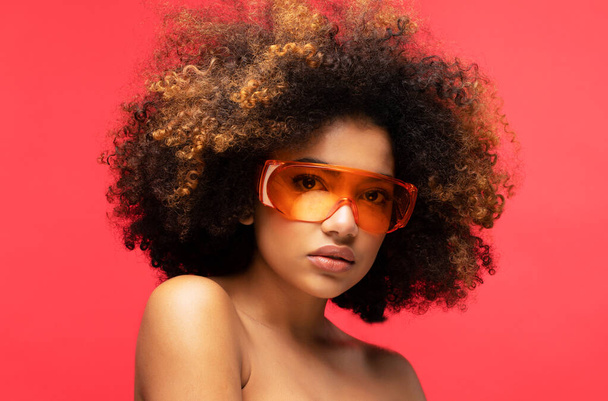 Young woman wearing sunglasses isolated on studio red background. Excited african american female. Close up portrait. - Фото, зображення