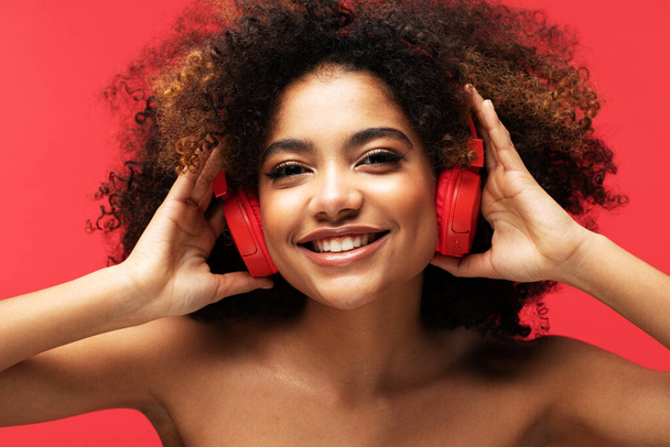 People, music, emotions concept. Young afro american female with dances in rhythm of melody. Portrait over red color background. - 写真・画像