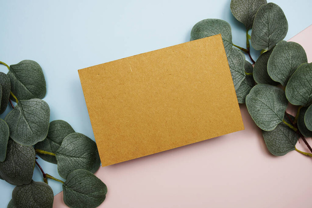 Empty invitation card mockup with green eucalyptus leaves on pink and blue background - Фото, зображення