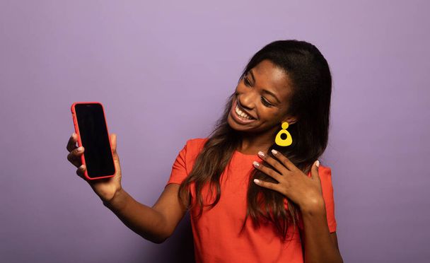 Portrait of positive young afro american woman promoter show smartphone over purple color background - Foto, Bild