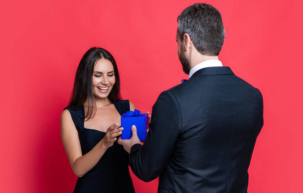cheerful love couple with present at studio. love couple with present on background. photo of love couple with present box. love couple with present isolated on red. - Fotó, kép