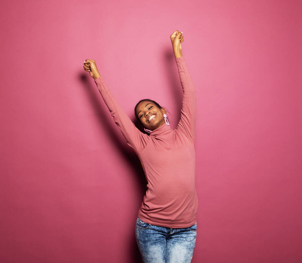 νεαρή ευτυχισμένη afro γυναίκα φορούν casual ρούχα χορό αναζητούν κενό χώρο απομονωμένο ροζ χρώμα φόντο - Φωτογραφία, εικόνα