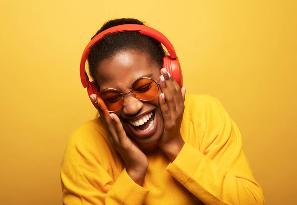 Young afro american female with dances in rhythm of melody. Portrait woman with headphones over yellow color background. - Zdjęcie, obraz