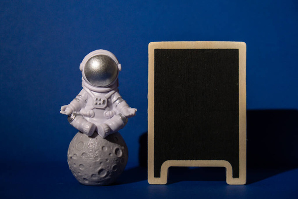 Plastic toy astronaut with blackboard template mock up for your text on colorful blue background Copy space. Concept of out of earth travel, private spaceman commercial flights. Space missions and - Fotó, kép