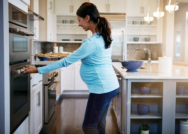 Выглядит очень вкусно. беременная женщина берет поднос с печеньем из духовки - Фото, изображение