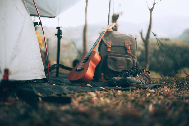 Kampeeruitrusting, tassen, schoenen, ukelele, statief naast de tent in de ochtend. Objectkamp, Reizen en roeping concept. - Foto, afbeelding