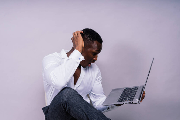 Optimistic african-american male student in a casual shirt using laptop pc isolated - Foto, Imagem