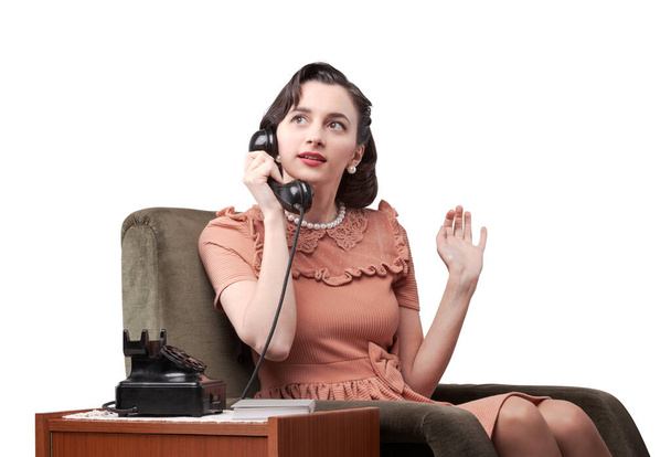 Vintage style woman sitting on an armchair and gossiping on the phone - Photo, image