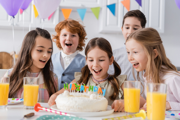 grupo de crianças espantadas olhando para bolo de aniversário com velas durante a festa em casa  - Foto, Imagem