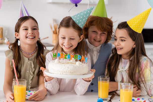 Glückliches Geburtstagskind mit Kuchen und Kerzen bei fröhlichen Freunden während der Feier zu Hause  - Foto, Bild
