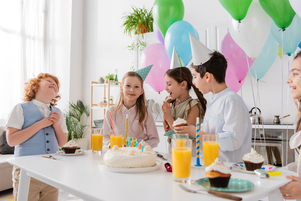 group of joyful children in party caps having fun during birthday party next to colorful balloons  - Photo, Image