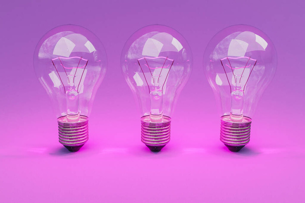three retro style lightbulbs with glowing filament standing in a row on infinite colorful background; creativity design concept; 3D Illustration - Фото, изображение